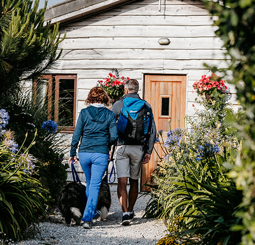 Couple and their dogs walking towards Adams Fish and Chips shop on St Martins, Isles of Scilly